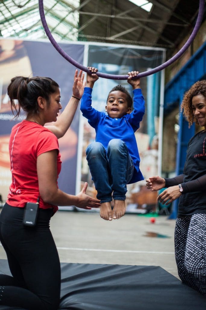 Two people are either side of a child, who is holding himself up on an aerial hoop.