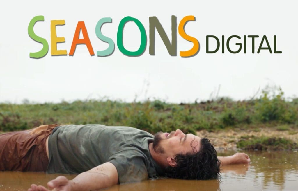 An acrobat lies on his back in the mud. words read 'seasons digital'