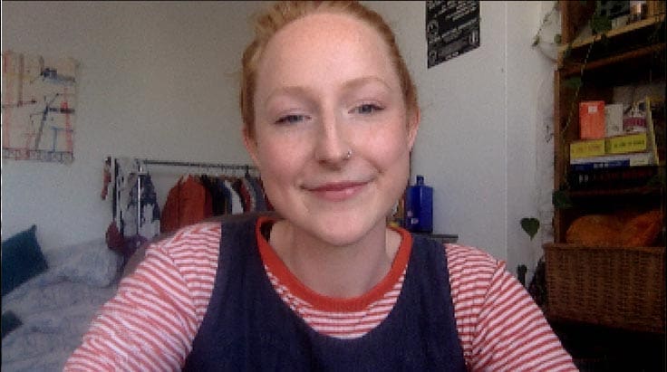 A woman smiling in a room, wearing a stripy top.