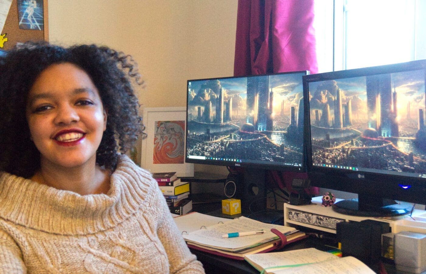 A mixed race woman sits in front of two computer screens, smiling.