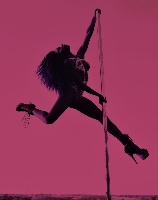 A woman wearing stilettos swings from a pole on a bright pink background.