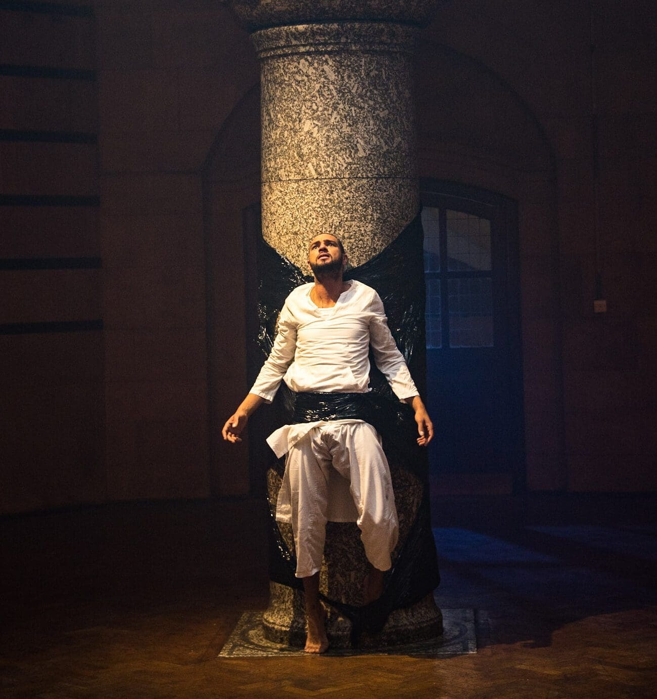 A man wearing white clothes is duct-taped to a large stone pillar