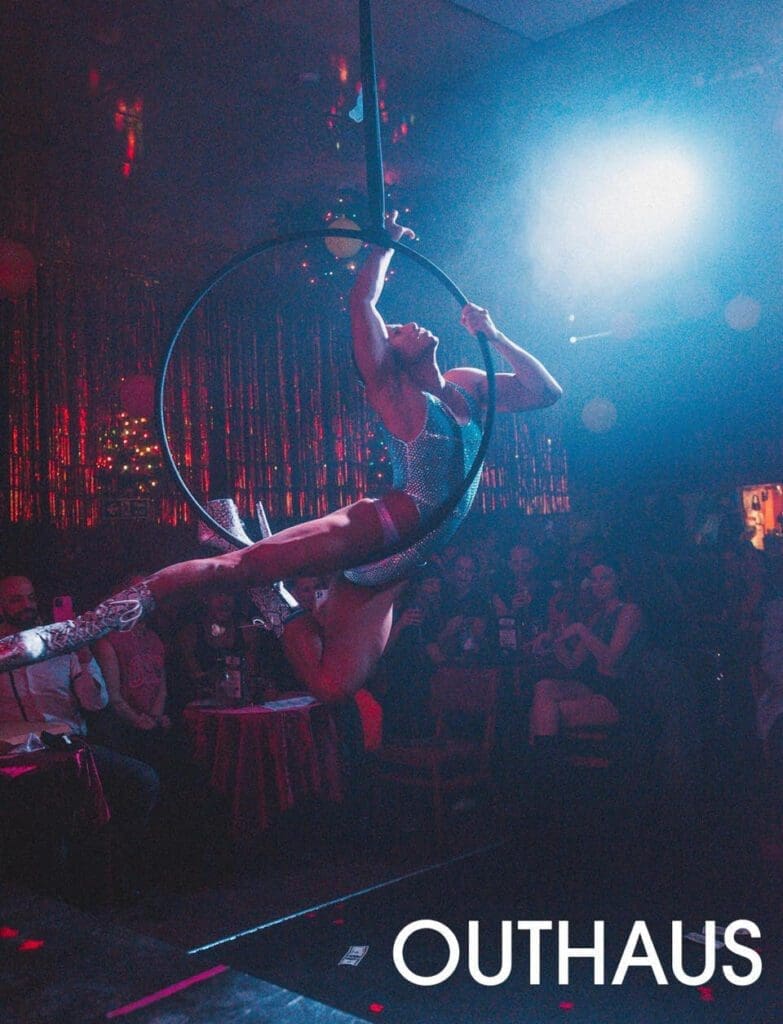 A performer balances on an aerial hoop under a bright spotlight on stage.