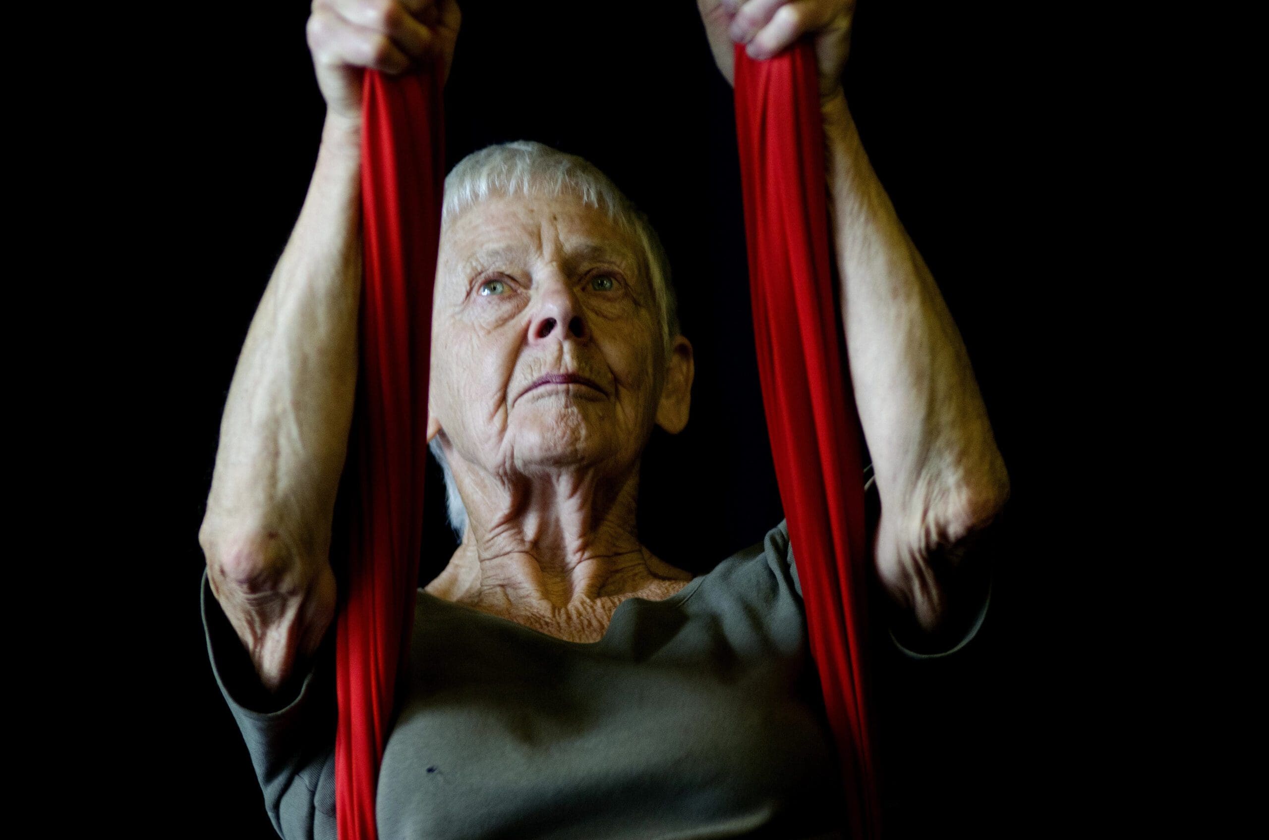 An elderly white woman with short grey hair is holding onto two aerial ropes.
