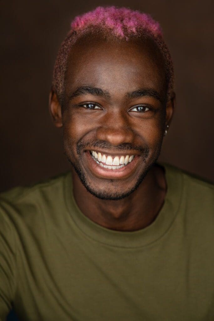 A close up of a man with pink hair, smiling and wearing a green shirt
