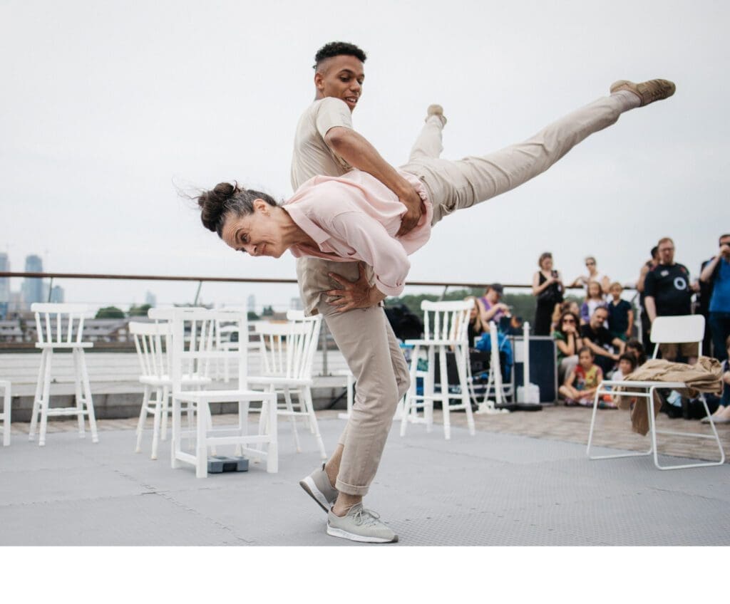 An older woman is flung into the air by a younger man in at outdoor performance space. They both smile