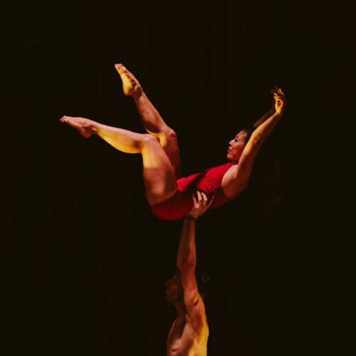 A woman is lifted into the air wearing a red leotard