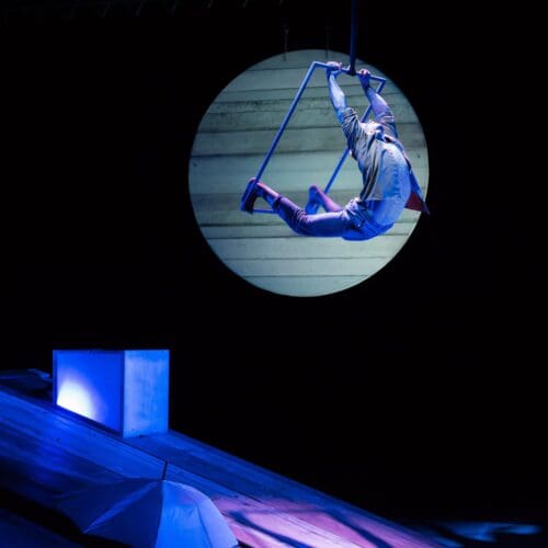 A performer swings on a trapeze high above a stage