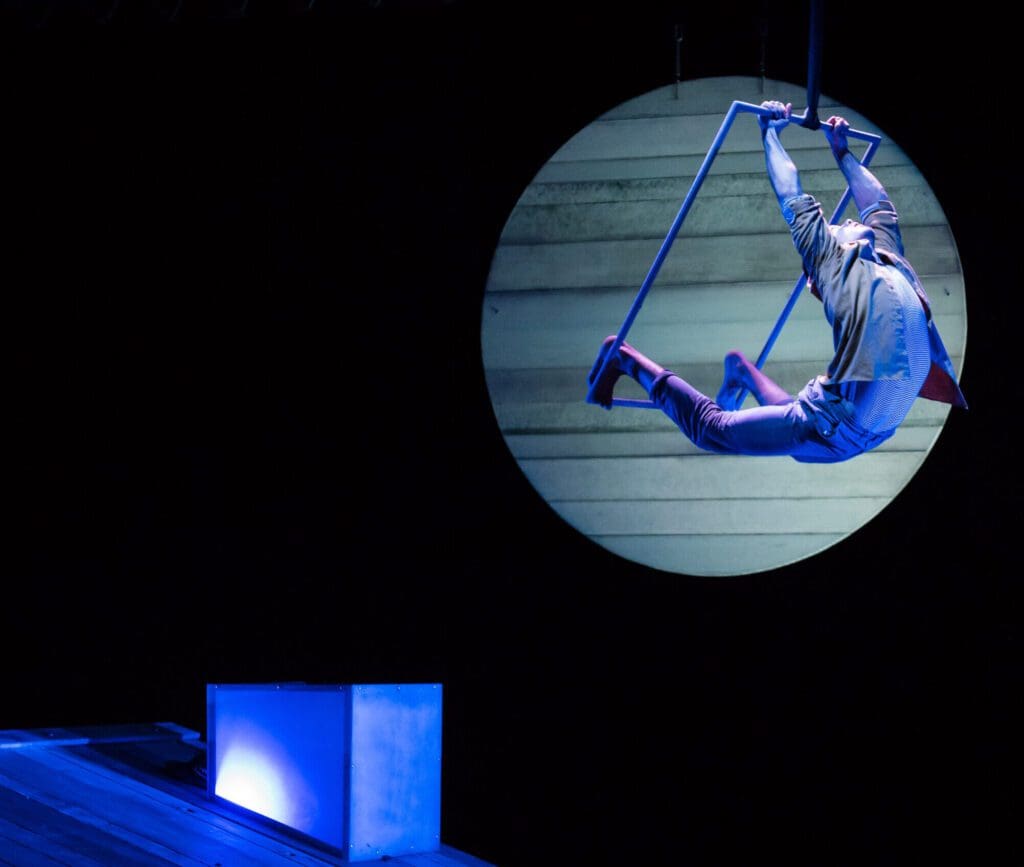 A performer swings on a trapeze high above a stage