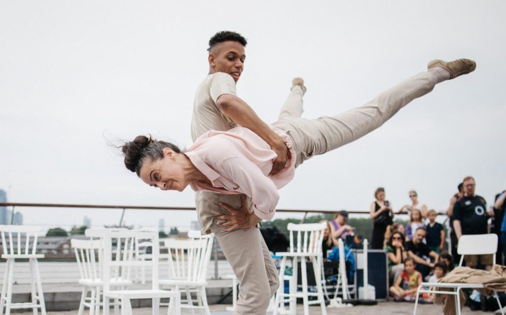 An older woman is flung into the air by a younger man in at outdoor performance space. They both smile