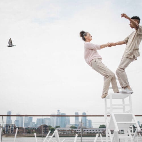 Two acrobats hold each others hands as they balance away from each other
