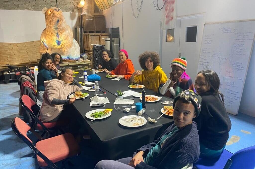 A group of people sit around a table in a group. They are in a rehearsal
