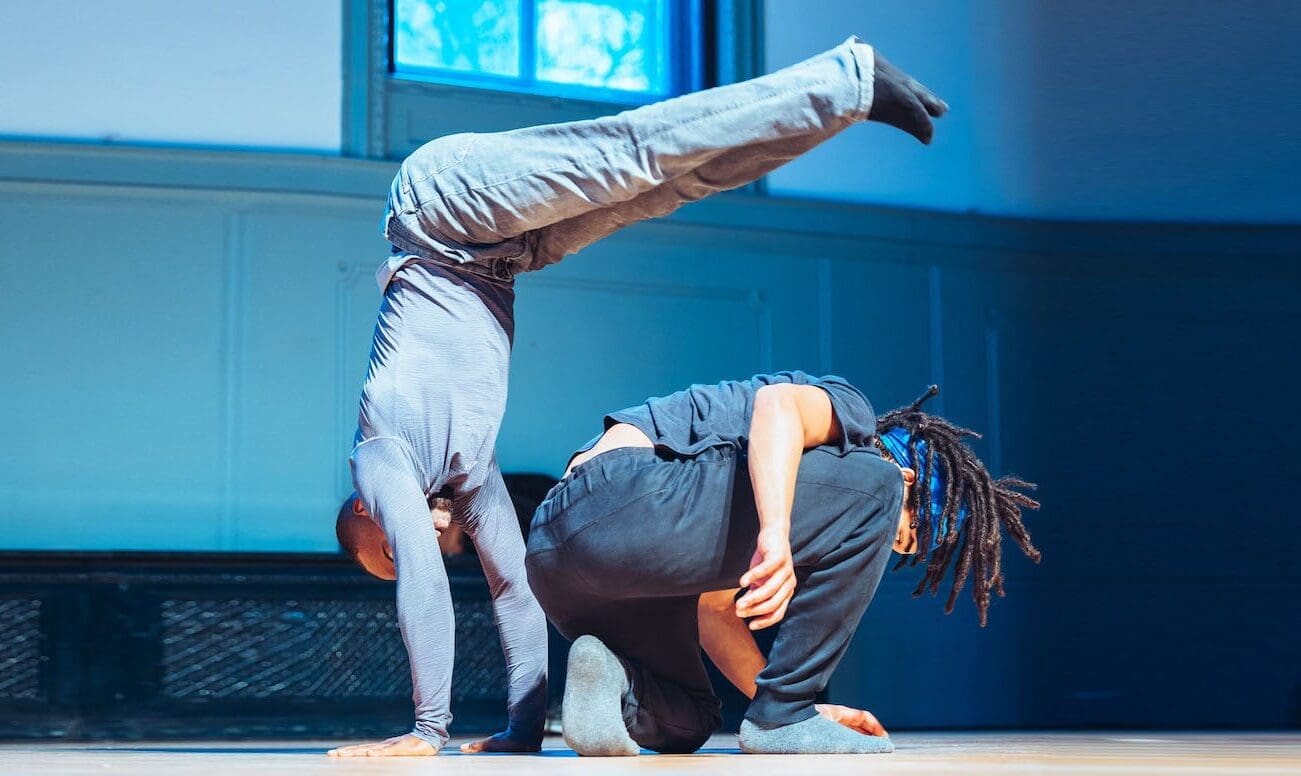 An acrobat jumps over another performer and lifts his legs in the air