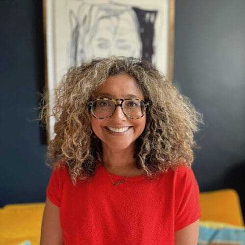 a white British, Indian and Malawian heritage wearing a red top with curly blonde brown hair and glasses