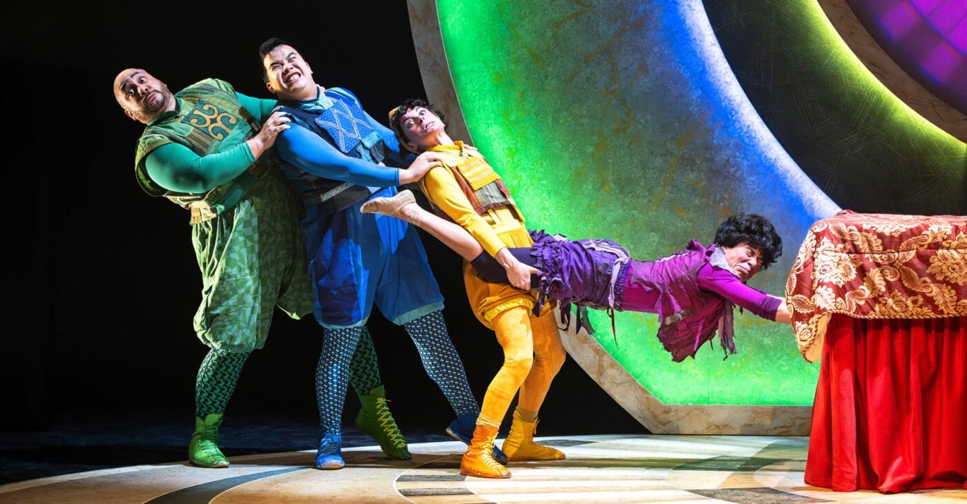 A group of acrobats pull each other from a pile of mattresses