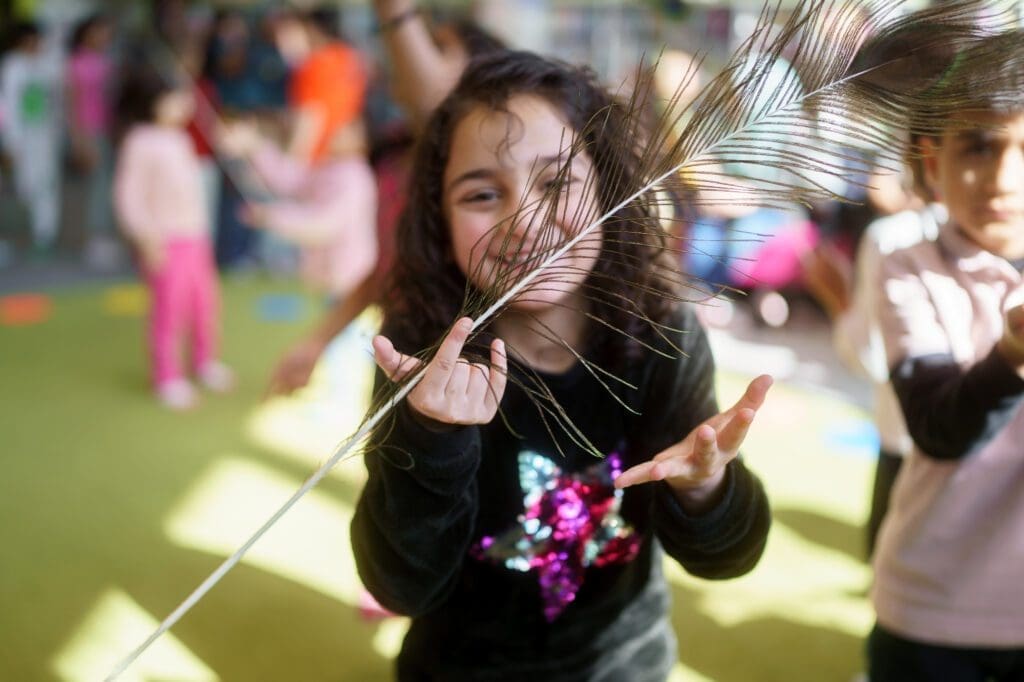 A young girl holds a peacock feather up to her face and smiles as she takes part in a seasons workshop