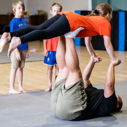 a teenage girl is lifted into the air as part of an acro circus skills class at a circus summer school in stoke on trent