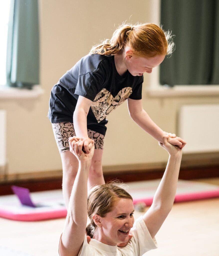 A young girl stands on a circus artists shoulders and holds onto her hands at a circus summer school in stoke on trent