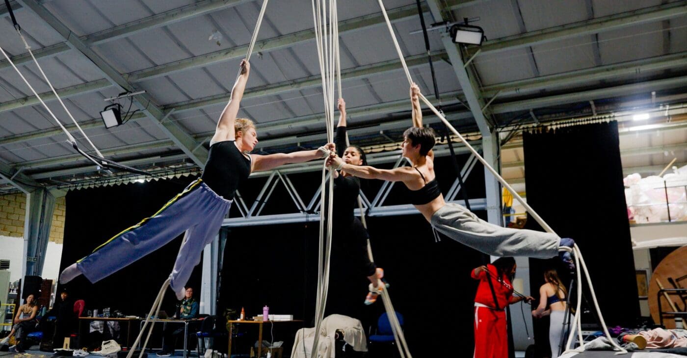 Three aerialists spins around in a circle on aerial ropes