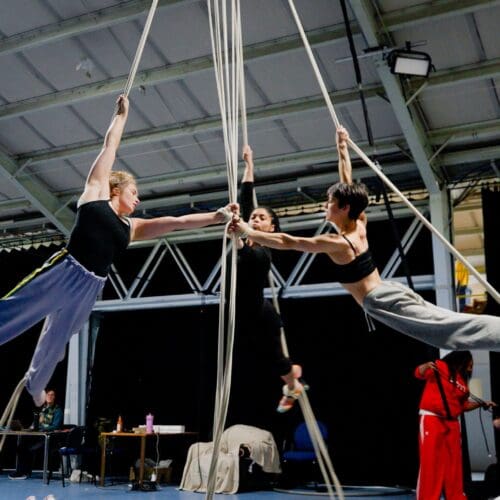 Three aerialists spins around in a circle on aerial ropes