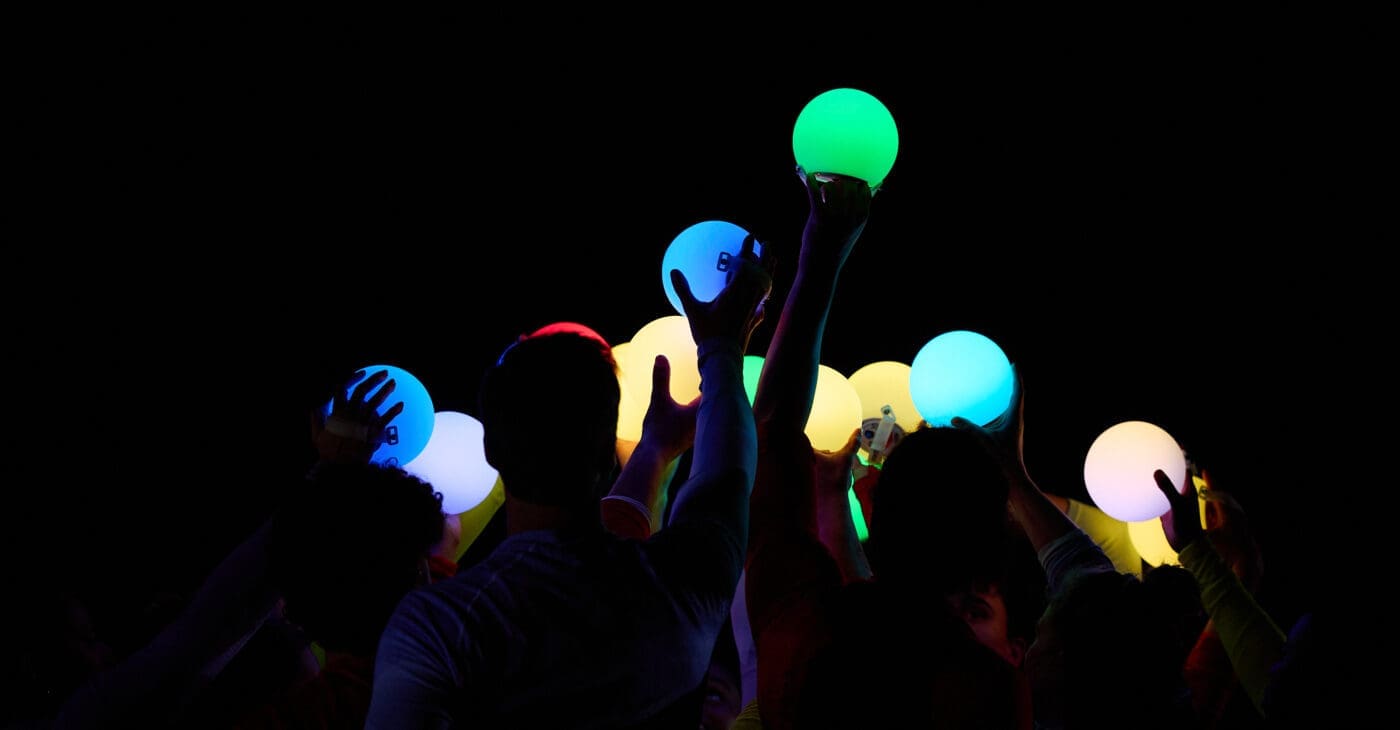 Hands reach up to a dark sky holding glowing orbs of light