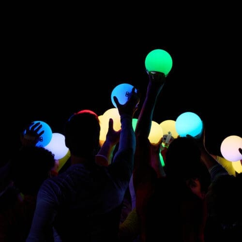 Hands reach up to a dark sky holding glowing orbs of light